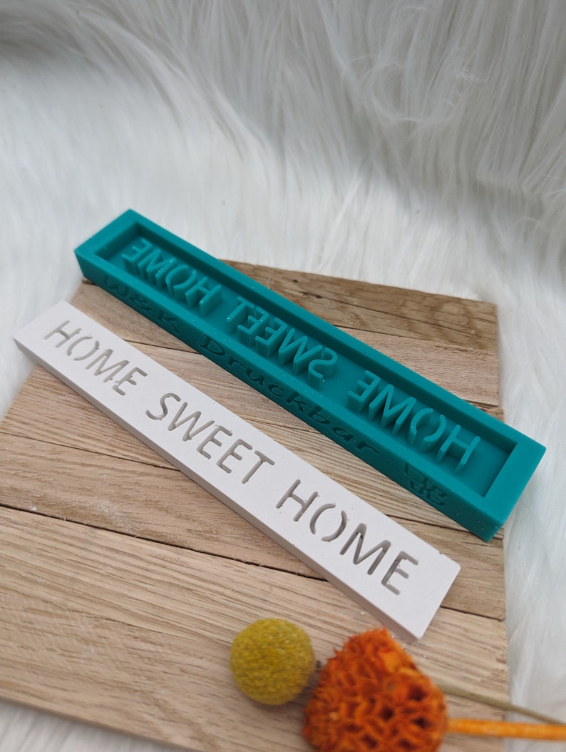 May include: Two rectangular signs with the text "Home Sweet Home" in raised letters. The top sign is teal and the bottom sign is white.