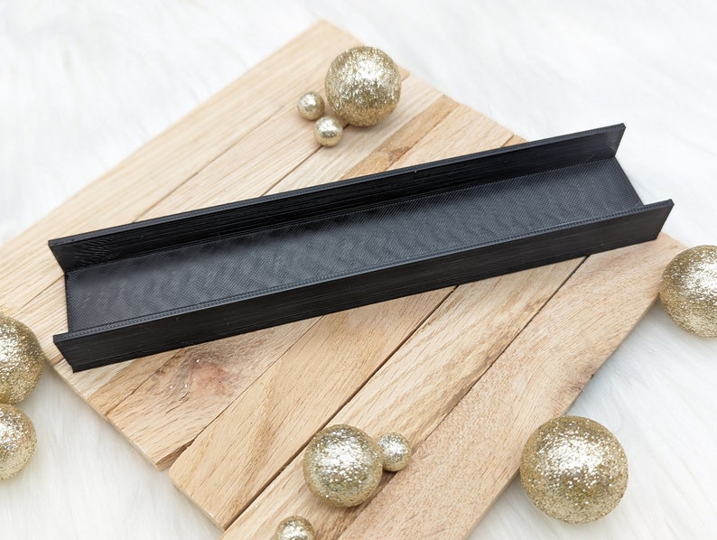 May include: Black plastic tray with a textured surface, resting on a wooden surface. The tray is surrounded by gold glitter balls.