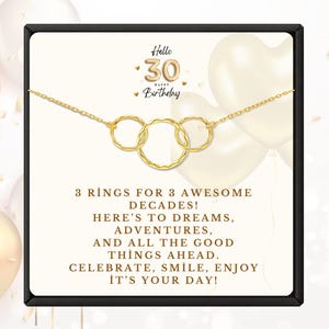 May include: A gold-colored necklace with three interlocking rings, presented on a card with the text "Hello 30 Happy Birthday." The card also includes the message "3 rings for 3 awesome decades!" and other celebratory text.