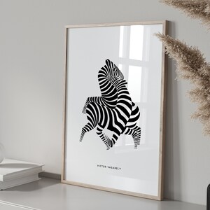 K&ouml;nnte beinhalten: Schwarz-wei&szlig;es abstraktes Kunst-Druckbild von zwei Zebras in einem geometrischen Muster. Der Druck ist in einem hellen Holzrahmen gerahmt und h&auml;ngt an einer wei&szlig;en Wand. Der Druck ist mit "Victor Vasarely" betitelt.