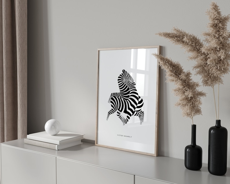 K&ouml;nnte beinhalten: Schwarz-wei&szlig;es abstraktes Kunst-Druckbild von zwei Zebras in einem geometrischen Muster. Der Druck ist in einem hellen Holzrahmen gerahmt und h&auml;ngt an einer wei&szlig;en Wand. Der Druck ist mit "Victor Vasarely" betitelt.