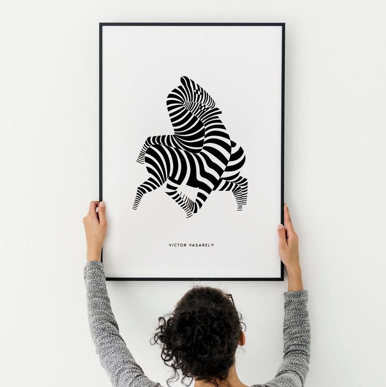 K&ouml;nnte beinhalten: Ein Schwarz-Wei&szlig;-Abstrakt-Kunstdruck mit einem Zebra-Muster. Der Druck ist in einem schwarzen Rahmen gerahmt und h&auml;ngt an einer wei&szlig;en Wand. Der Name des K&uuml;nstlers, "VICTOR VASARELY", ist unter dem Bild gedruckt.