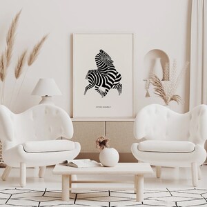 K&ouml;nnte beinhalten: Ein abstrakter Zebra-Kunstdruck in Schwarzwei&szlig; in einem wei&szlig;en Rahmen, der an einer wei&szlig;en Wand &uuml;ber einem wei&szlig;en Sofa h&auml;ngt. Der Druck ist mit "Victor Vasarely" betitelt.