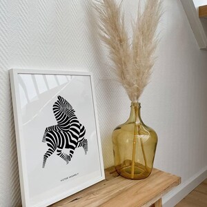 K&ouml;nnte beinhalten: Ein schwarz-wei&szlig;er abstrakter Zebra-Druck in einem wei&szlig;en Rahmen, der an einer wei&szlig;en Wand h&auml;ngt. Eine Vase mit getrocknetem Pampasgras steht auf einem Holztisch.