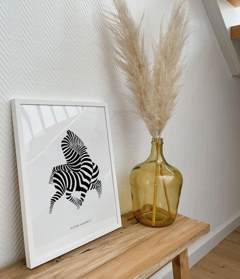 K&ouml;nnte beinhalten: Ein schwarz-wei&szlig;er abstrakter Zebra-Druck in einem wei&szlig;en Rahmen, der an einer wei&szlig;en Wand h&auml;ngt. Eine Vase mit getrocknetem Pampasgras steht auf einem Holztisch.