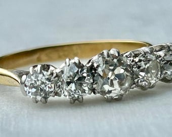 Könnte beinhalten: Ein Goldring mit fünf runden Diamanten, die in einer Reihe angeordnet sind. Die Diamanten sind klar und haben einen leichten Glanz.