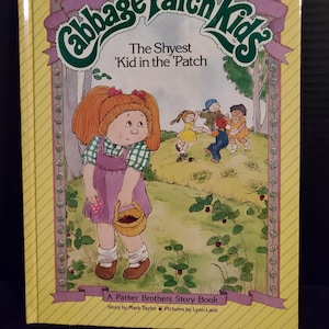 May include: A vintage Cabbage Patch Kids storybook titled "The Shyest 'Kid in the 'Patch." The cover features a cartoon illustration of a girl with red hair, wearing a purple dress and holding a basket. Other children are playing in the background.