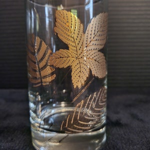 May include: A clear glass tumbler with a gold leaf design. The leaves are stylized and have a dotted pattern.