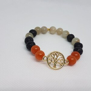 Könnte beinhalten: Ein Armband aus orangefarbenen, grauen und schwarzen Perlen mit einem goldenen Lebensbaum-Anhänger.