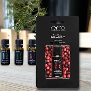 Puede incluir: Un paquete blanco y negro con una pequeña botella de aroma de sauna de bayas árticas. La botella está etiquetada con "rento" y "SAUNA SCENT". El paquete está rodeado de bayas rojas.