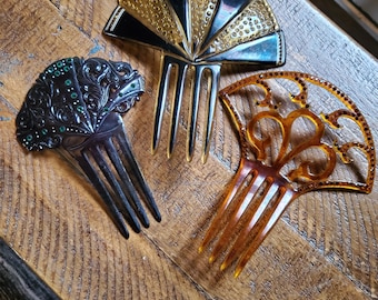 May include: Three vintage hair combs with decorative designs. The combs are made of black, brown, and gold plastic. The black comb has green rhinestones. The brown comb has a floral design. The gold comb has a fan-shaped design.