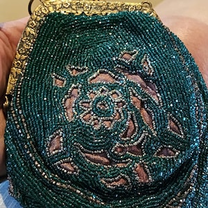 May include: A small, vintage-style coin purse featuring intricate dark green beadwork over a soft mauve fabric base. The purse is framed by an ornate, antique-gold colored metal clasp with a floral embossed pattern and a decorative top closure.