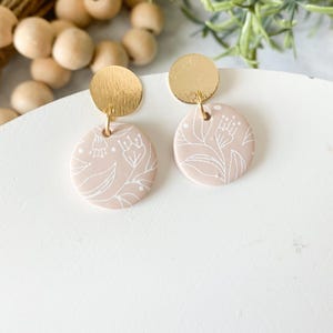 May include: A pair of gold and blush pink earrings with a floral pattern. The earrings are made of polymer clay and have a gold-toned metal hook.