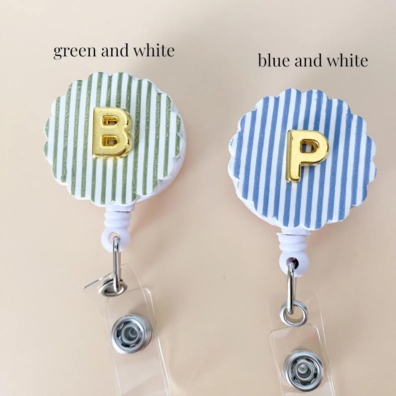 Puede incluir: Dos portatarjetas retr&aacute;ctiles con bordes festoneados. Uno presenta rayas verticales verdes y blancas con una letra B dorada, y el otro rayas verticales azules y blancas con una letra P dorada. Ambos tienen carcasas y clips de pl&aacute;stico blanco.