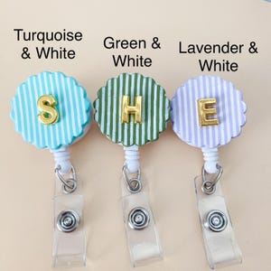 Puede incluir: Tres portatarjetas con bordes festoneados y rayas verticales en turquesa, verde y lavanda, cada una combinada con blanco. Las letras doradas S, H y E est&aacute;n centradas en cada carrete. Las etiquetas dicen Turquoise & White, Green & White y Lavender & White.