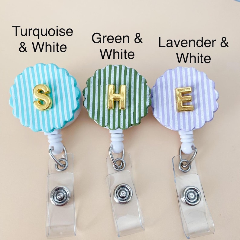 Puede incluir: Tres portatarjetas con bordes festoneados y rayas verticales en turquesa, verde y lavanda, cada una combinada con blanco. Las letras doradas S, H y E est&aacute;n centradas en cada carrete. Las etiquetas dicen Turquoise & White, Green & White y Lavender & White.