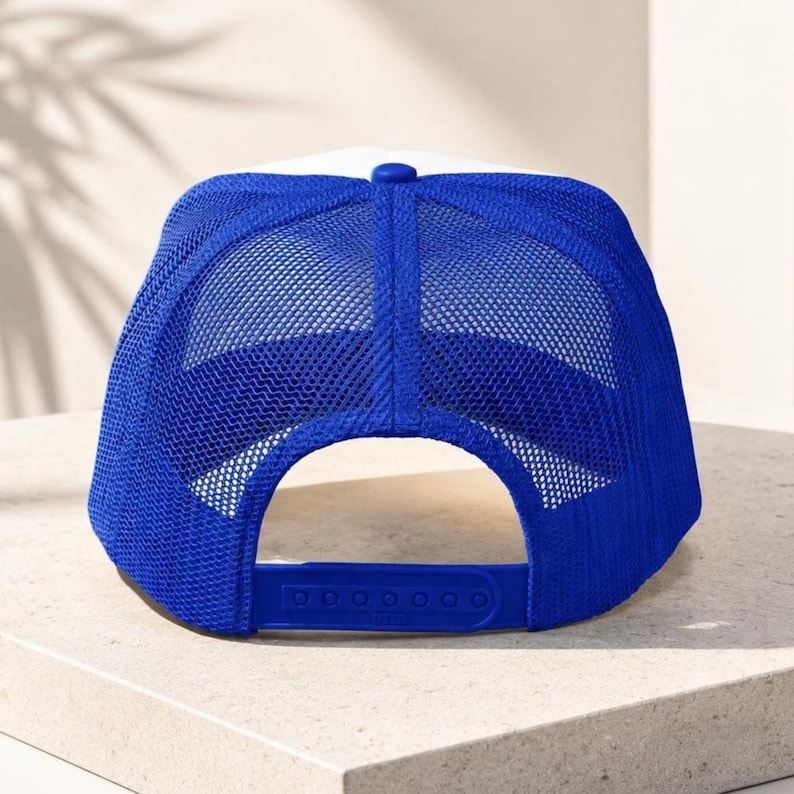 May include: A baseball cap featuring a white front panel and a vibrant blue mesh back. The cap includes a matching blue plastic snapback closure at the rear, allowing for adjustable sizing. The design incorporates a structured crown and a breathable mesh.