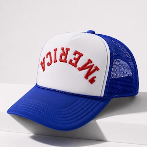 May include: A blue and white trucker cap featuring a foam front panel with the word MERICA embroidered in red capital letters in an arched design. The cap includes a solid blue brim and a breathable blue mesh back with an adjustable snap closure.