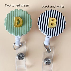 Puede incluir: Dos portatarjetas con bordes festoneados. Uno presenta un patr&oacute;n de rayas verdes en dos tonos con una letra D dorada, y el otro tiene un patr&oacute;n de rayas blancas y negras con una letra B dorada. Ambos incluyen una carcasa de pl&aacute;stico blanco.