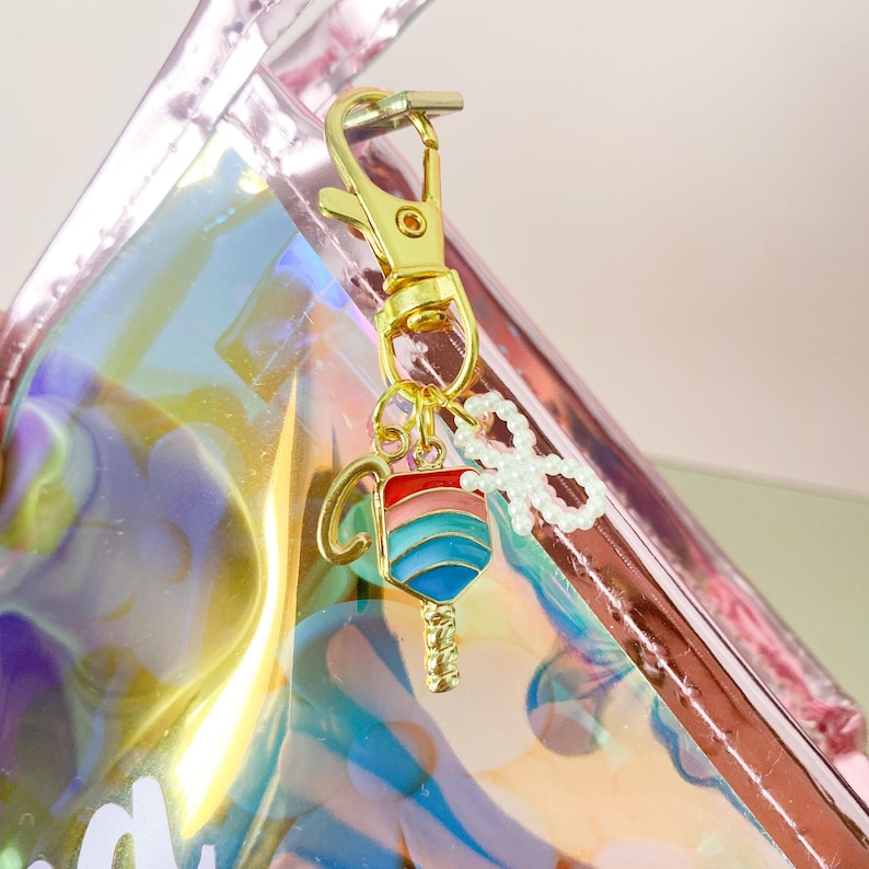May include: A gold-colored keychain with a blue, red, and white striped lollipop charm and a white pearl bow charm.