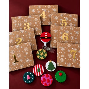 Pode incluir: Sete envelopes castanhos com padrões de flocos de neve brancos e números dourados de um a sete, um porta-crachá de cinto de Pai Natal vermelho e preto, e cinco ornamentos circulares de argila com árvores de Natal, corações e padrões.