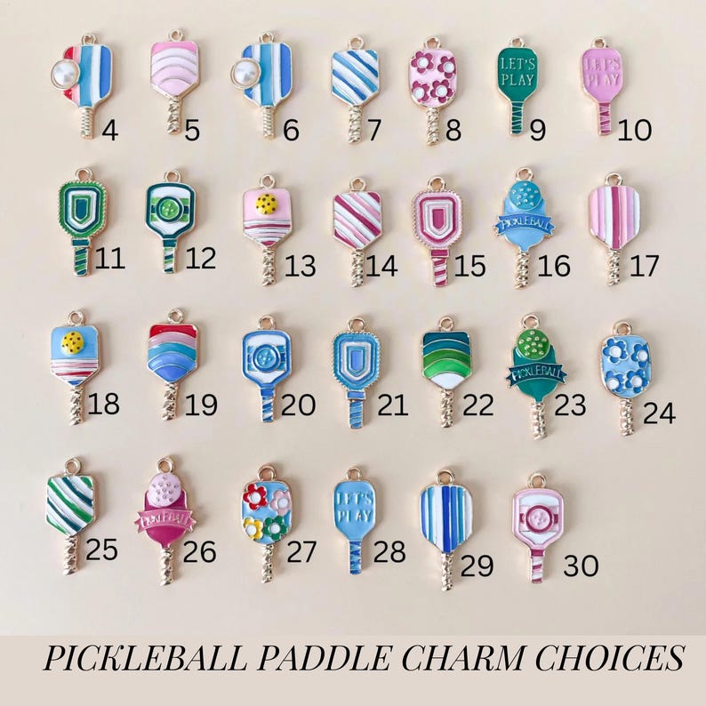 May include: Thirty different pickleball paddle charms with various designs and colors. The charms are made of metal and have a gold finish. Some of the designs include flowers, stripes, polka dots, and the words "Let's Play".