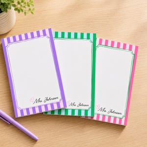 May include: Three rectangular notepads with vertical stripes in purple, green, and pink. Each notepad features a white center with a decorative border, a small pink heart icon, and the printed text Mrs. Johnson in a black cursive script font.