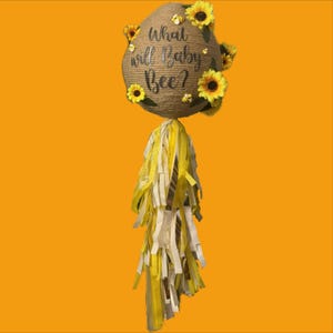 May include: A burlap and sunflower themed gender reveal party decoration with the text "What will baby bee?"