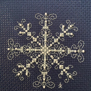 May include: A white snowflake embroidered on a dark blue fabric with white beads outlining the snowflake.