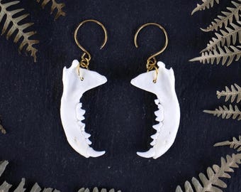 May include: A pair of gold hoop earrings with white bone jawbone pendants. The jawbones have teeth and are a unique and edgy accessory.