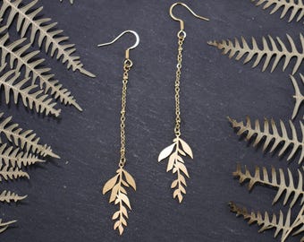 May include: A pair of gold dangle earrings with a delicate leaf design. The earrings are made of a thin chain with small beads and feature a cluster of leaves at the bottom.