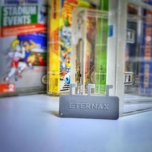以下が含まれることがあります： 「ETERNAX」と印刷された灰色のプラスチック製カートリッジホルダー。ホルダーは、ビデオゲームカートリッジを保管および表示するために設計されています。