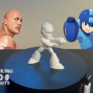 May include: A white 3D printed action figure of Mega Man, a video game character, standing on a black circular base. The figure is holding a weapon in its right hand. The background includes a cartoon image of Mega Man and a photo of Dwayne Johnson.
