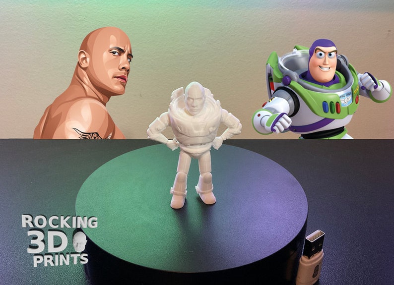 Op de afbeelding: Een wit 3D-geprint beeldje van Buzz Lightyear uit de Toy Story-franchise, staand met de handen op de heupen. Het beeldje staat op een zwart rond platform met de tekst "ROCKING 3D PRINTS" zichtbaar op de achtergrond.