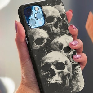 Puede incluir: Funda de teléfono negra con un gráfico de varios cráneos blancos sobre un fondo negro.