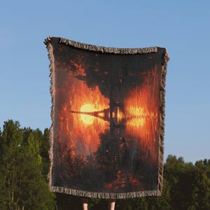 Puede incluir: Una manta de tejido de tapiz que presenta una escena de puesta de sol con la Torre Eiffel reflejada en un cuerpo de agua. La manta tiene un borde de flecos.