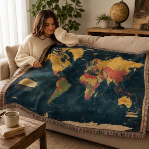 Puede incluir: Una manta tejida que presenta un diseño detallado de mapa mundial con un fondo de océano azul oscuro y continentes representados en tonos amarillos, rojos y verdes. La manta tiene un borde con flecos e incluye texto impreso a la izquierda.