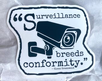 May include: A white sticker with a black silhouette of a surveillance camera and the text "Surveillance breeds conformity." - Glenn Greenwald.