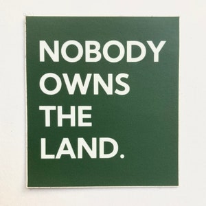 May include: A dark green square sticker with white text that reads "NOBODY OWNS THE LAND."