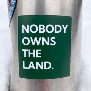 May include: A green sticker with white text that reads "NOBODY OWNS THE LAND."