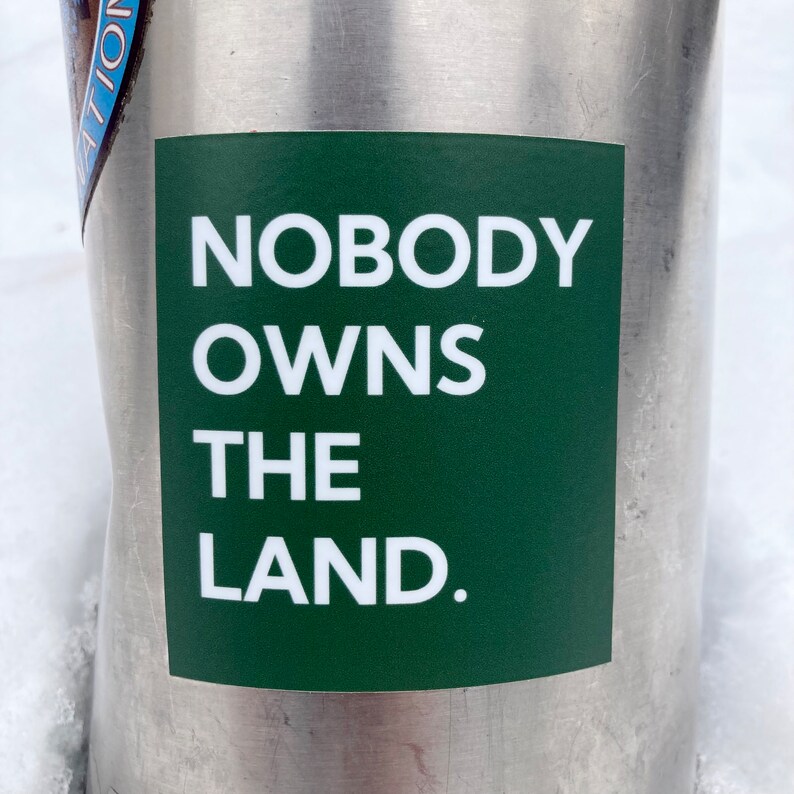 May include: A green sticker with white text that reads "NOBODY OWNS THE LAND."
