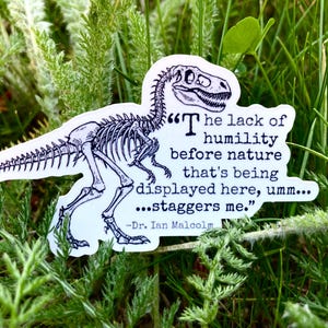 May include: A white sticker featuring a black and white dinosaur skeleton with the quote "The lack of humility before nature that's being displayed here, umm... staggers me." by Dr. Ian Malcolm. The sticker is set against a backdrop of green grass and foliage.
