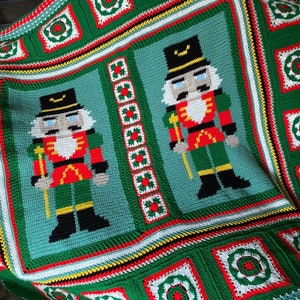 May include: A green, red, and white crocheted blanket with a repeating pattern of nutcracker figures and wreaths.