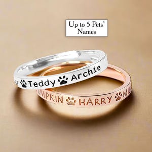 Puede incluir: Dos anillos de plata y oro rosa con huellas de pata grabadas y los nombres "Teddy", "Archie", "Pumpkin" y "Harry".
