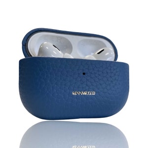 Puede incluir: Una funda de cuero azul para Apple AirPods Pro con la palabra "MO&NREED" grabada en la parte delantera.