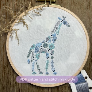 May include: A blue and green floral embroidered giraffe design on a white fabric stretched in a wooden embroidery hoop. The text "PDF pattern and stitching guide" is visible below the hoop.