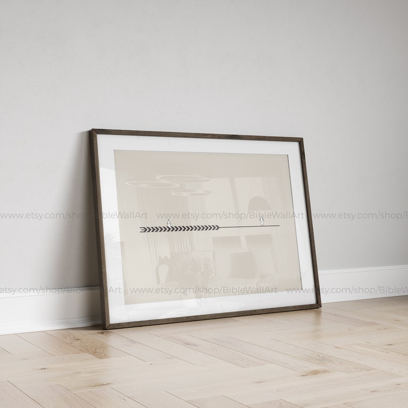 May include: A framed print with a minimalist design featuring a beige background with a black arrow and geometric shapes. The print is in a brown frame and is sitting on a light wood floor.