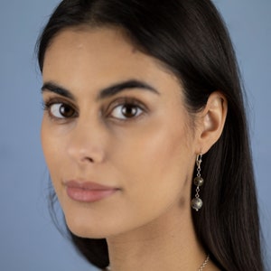 May include: A woman with long dark hair is wearing a pair of silver dangle earrings with dark grey and black round beads.