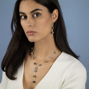 May include: A silver necklace and earrings with a y-shaped pendant and multiple small, round, gray, brown, and black stones.