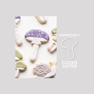 May include: A collection of decorated sugar biscuits shaped like mushrooms and a snail, featuring purple, green, and white icing. The text MUSHROOM 1 COOKIE CUTTER is displayed next to a white outline drawing of a mushroom shape on a plain background.